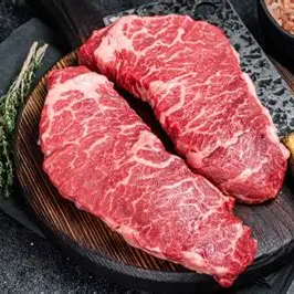 Two raw denver steaks on a dark surface with rosemary and a knife.